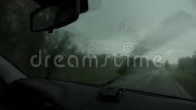 在恶劣的雨天驾驶，在汽车行驶过程中通过挡风玻璃观看乡村道路。 窗外的雨滴
